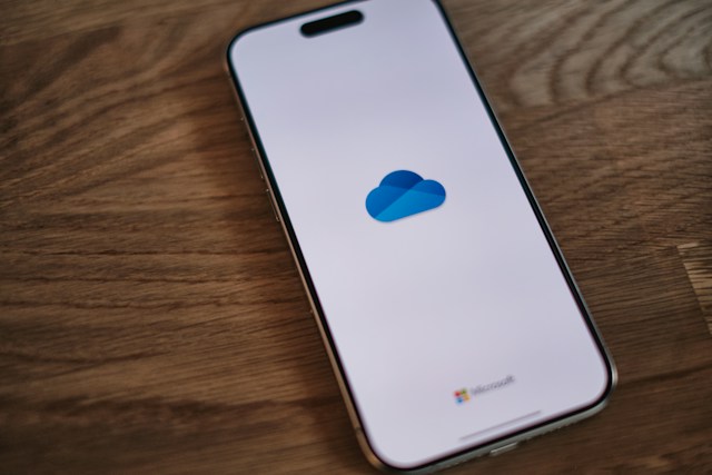 Smartphone op een houten tafel met het Microsoft OneDrive-logo op het scherm.
